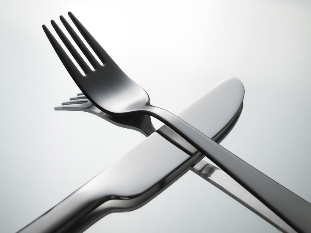 A knife and a fork crossed on a mirror surface.
