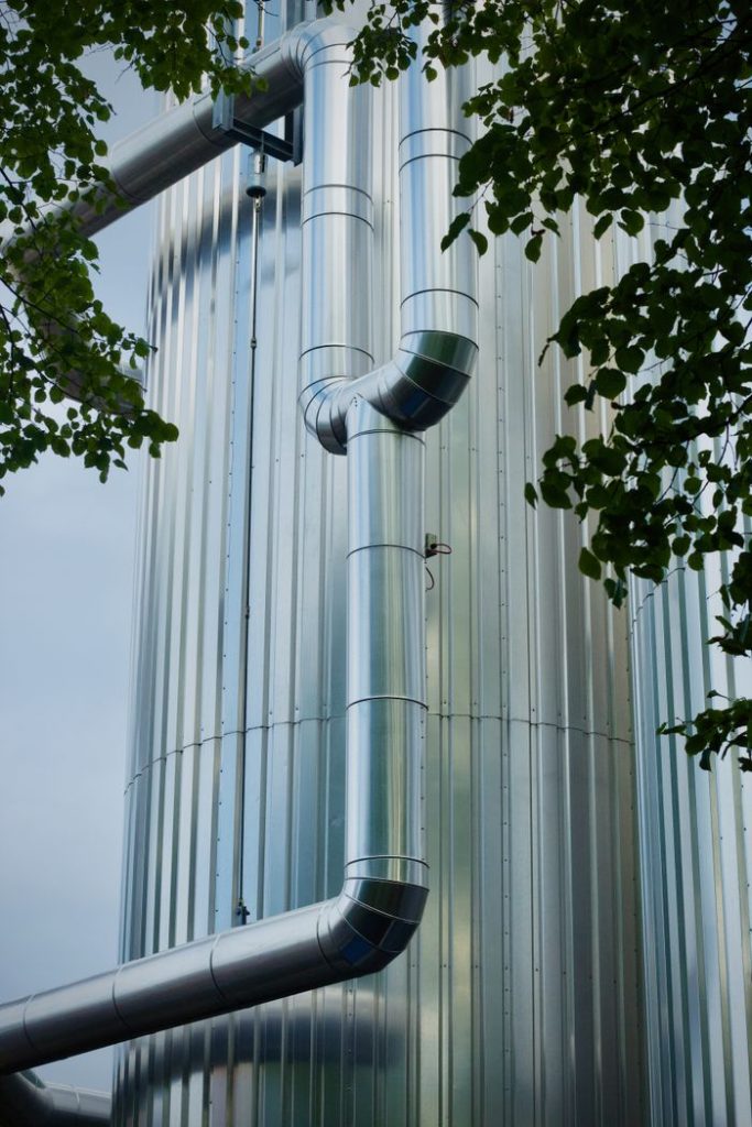 View of shiny metal pipes on an industrial tower framed by leaves.